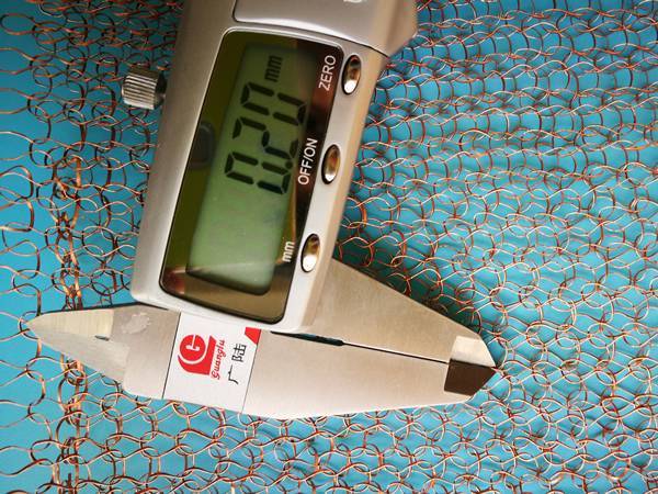 A caliper is measuring flat wire thickness of knitted copper mesh.