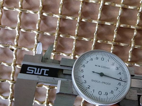 A caliper measuring the opening of crimped brass wire mesh.