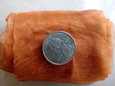 A roll of copper woven mesh with a metal coin.