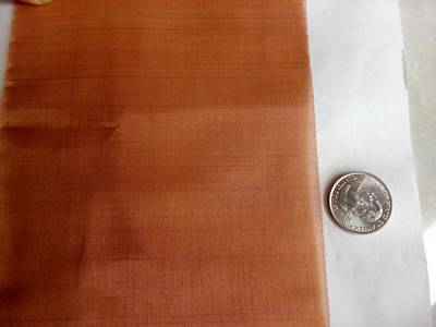 A piece of copper mesh is beside a metal coin.