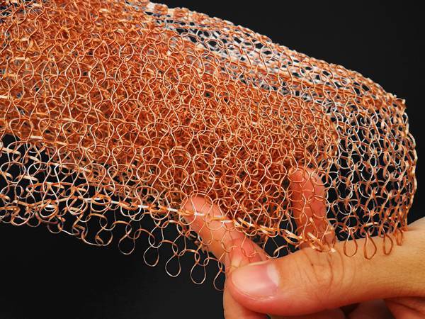 A hand is holding a piece of single flat wire single layer knitted copper mesh.