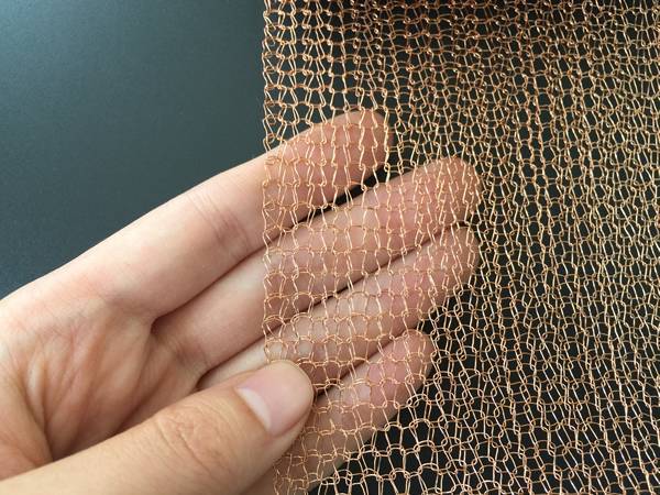 A hand is holding a piece of single layer double round wire knitted copper mesh.