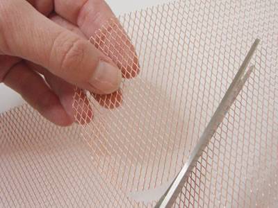 A piece of expanded copper mesh is being cut by a scissor.