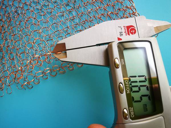 A caliper is measuring flat wire width of knitted copper mesh.
