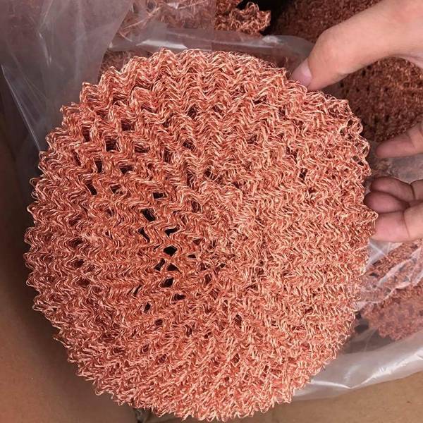 A hand is holding a roll of ginning type copper knitted mesh.