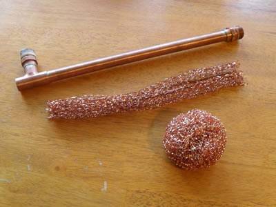 A roll of knitted copper mesh, a copper mechanical part and a cleaning ball on the table.