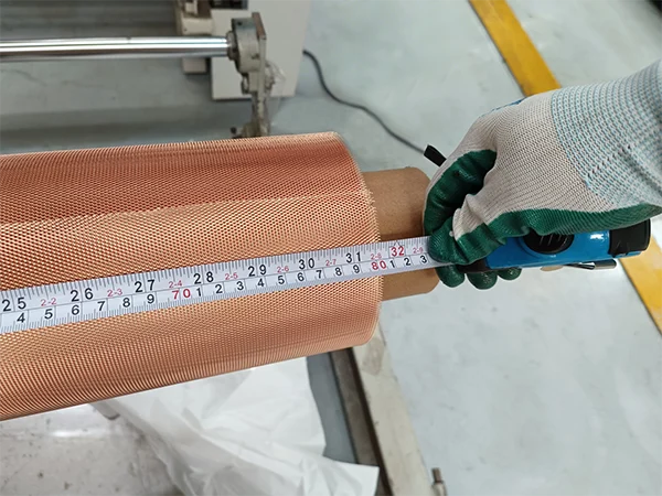 The worker measures the length of micro expanded copper mesh with a tape.