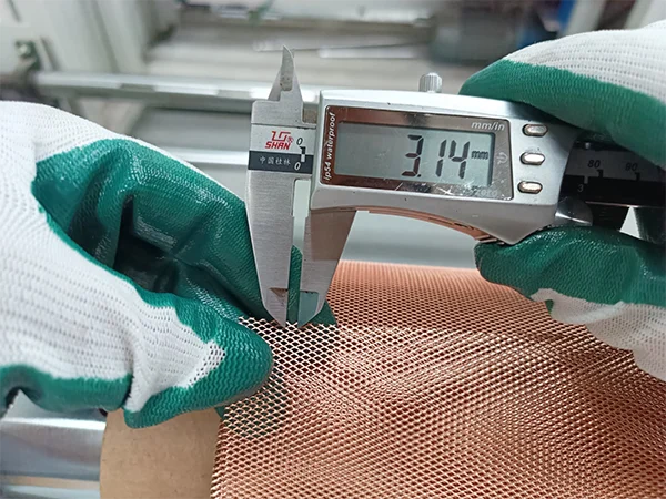 The worker measures the LWD of micro expanded copper mesh with a caliper.