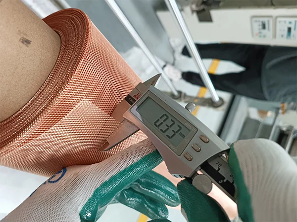 The worker measures the thickness of micro expanded copper mesh with a caliper.